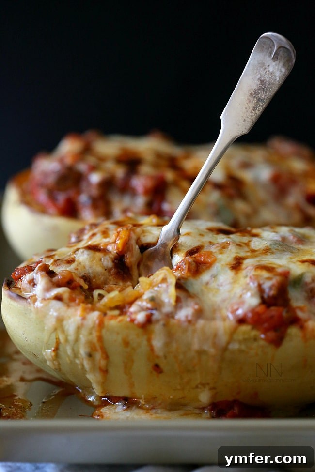 Savory Sausage and Pepper Spaghetti Squash Bake 4 A close-up shot of a half of Sausage and Peppers Stuffed Spaghetti Squash, with a fork gently pulling apart its cheesy, flavorful topping. The strands of spaghetti squash are visible, coated in the rich, savory filling.
