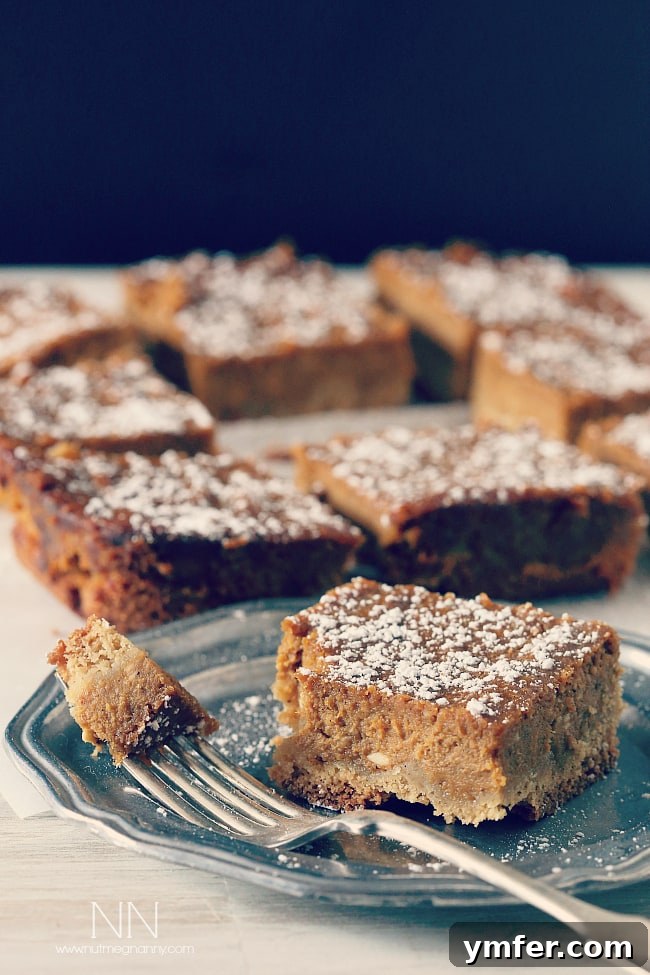 Delectable Pumpkin Pie Cake Bars, ready for your festive table. A generous serving of Pumpkin Pie Cake Bars on a white plate, with a background of more sliced bars, highlighting their autumnal appeal.