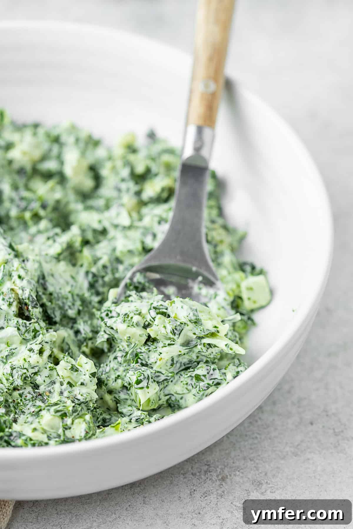 This totally simple creamed kale is the perfect Thanksgiving side dish. Full of healthy kale, cream cheese and a sprinkling of Parmesan cheese. Hello delicious! Creamed Kale in a bowl with a serving spoon.