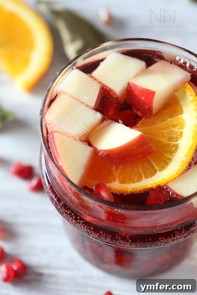 Fall-Inspired Red Wine Sangria A close-up shot of a glass of Thanksgiving sangria, showing sliced fruit and pomegranate seeds, indicating a refreshing and festive drink.