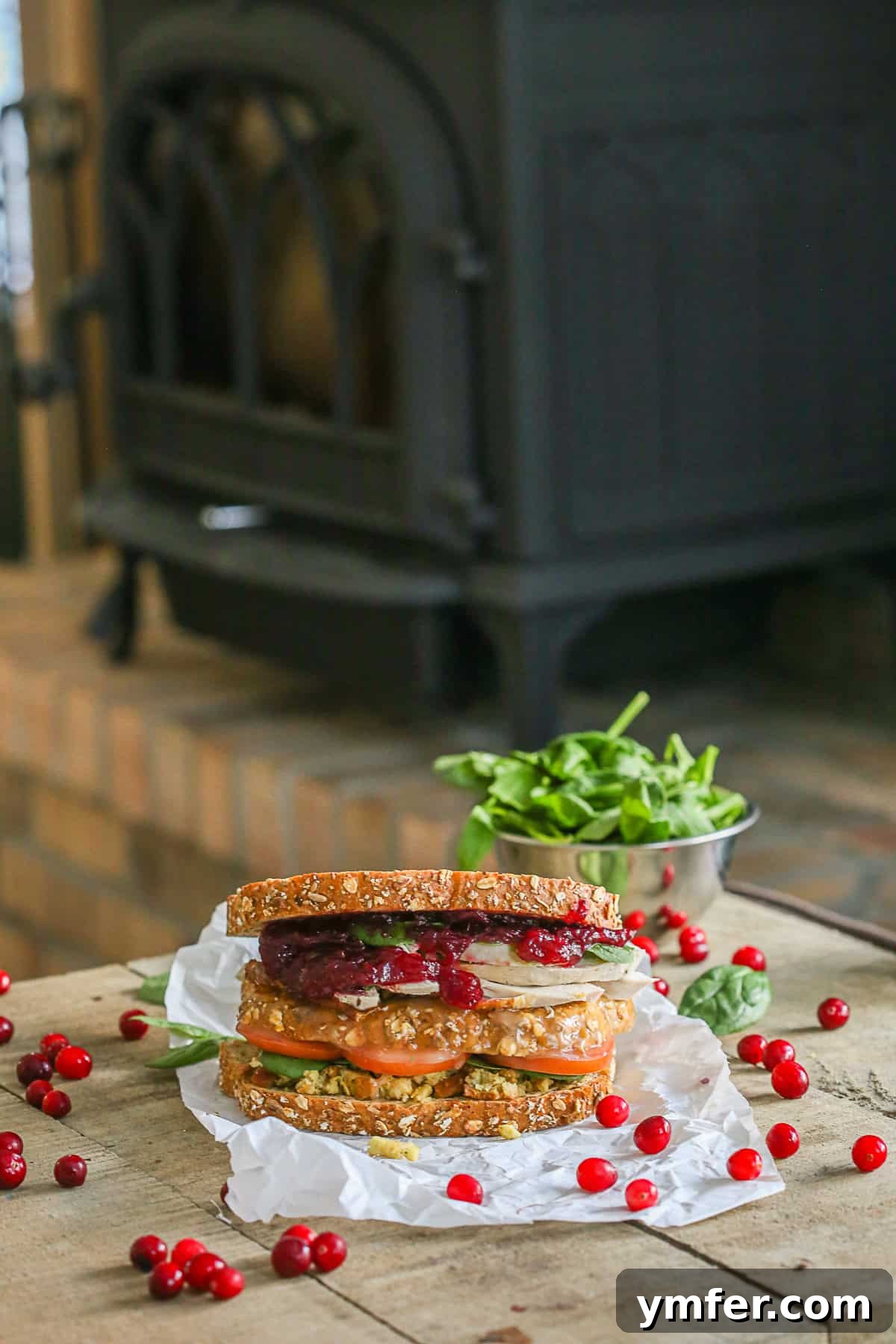 The Legendary Leftover Thanksgiving Moist Maker Sandwich 2 A delectable Leftover Thanksgiving Sandwich resting on a rustic wooden table, with a bowl of fresh spinach leaves blurred in the background, hinting at the fresh ingredients.