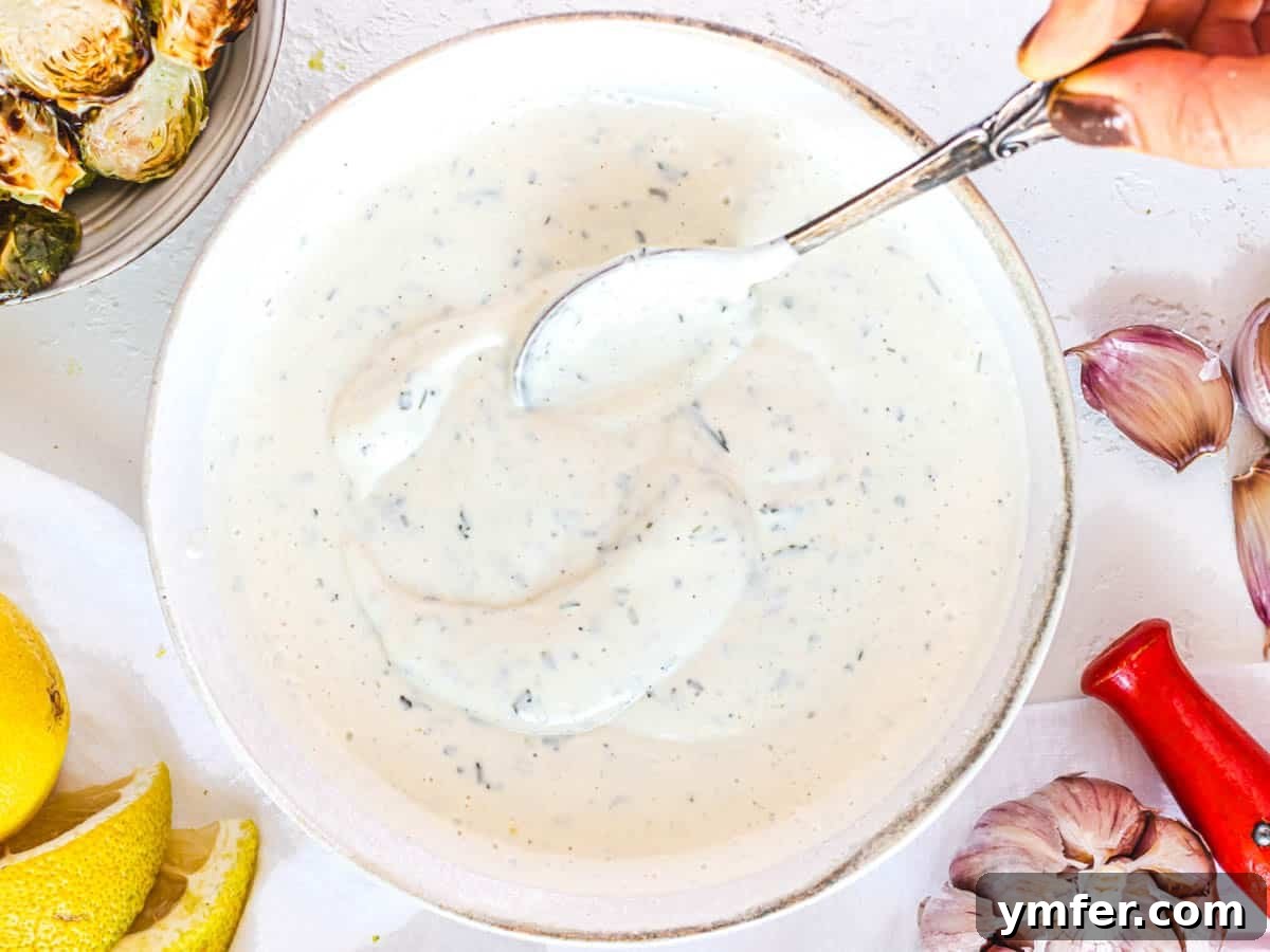 Creamy Vegan Ranch 5 A hand holding a silver spoon dipping into a bowl of creamy vegan ranch dressing.