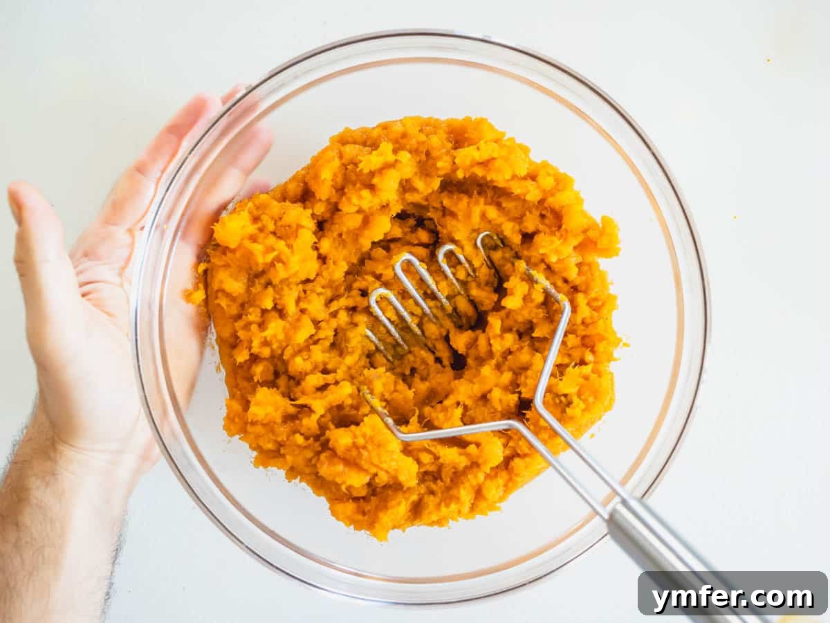 Golden Vegan Sweet Potato Delight 6 A bowl of creamy sweet potato mash with a potato masher, showing the process of combining ingredients for the casserole base