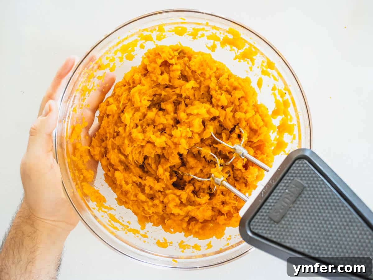 Golden Vegan Sweet Potato Delight 7 A close-up of a hand mixer creating smooth, fluffy sweet potato mash in a clear glass bowl, ensuring a uniform consistency
