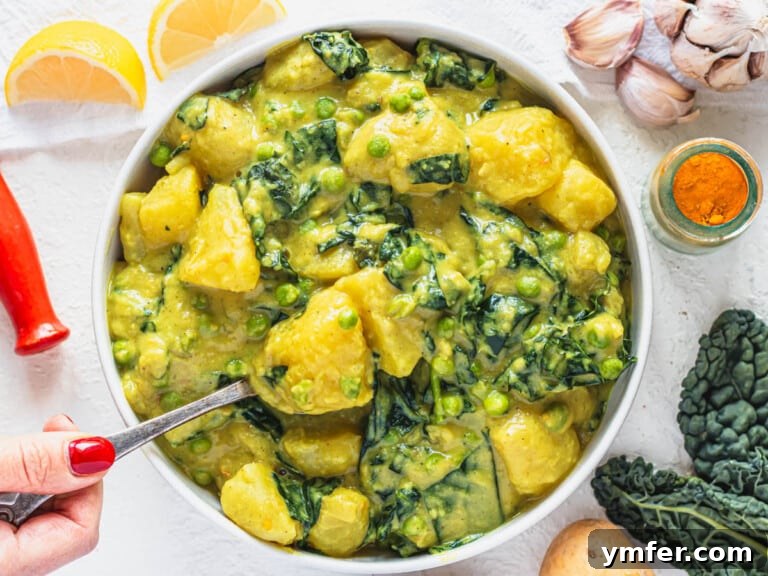 A perfectly cooked bowl of potato curry, garnished with fresh herbs and a hand reaching for a piece of naan.