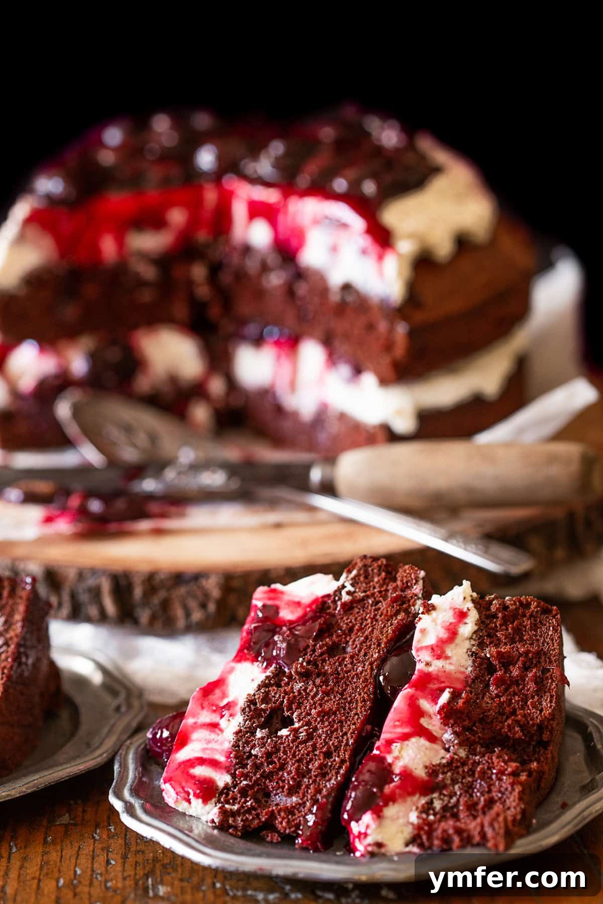 A perfectly sliced Black Forest Cake on a pewter plate, revealing its beautiful layers of dark chocolate cake, ruby-red cherry filling, and fluffy white cream.