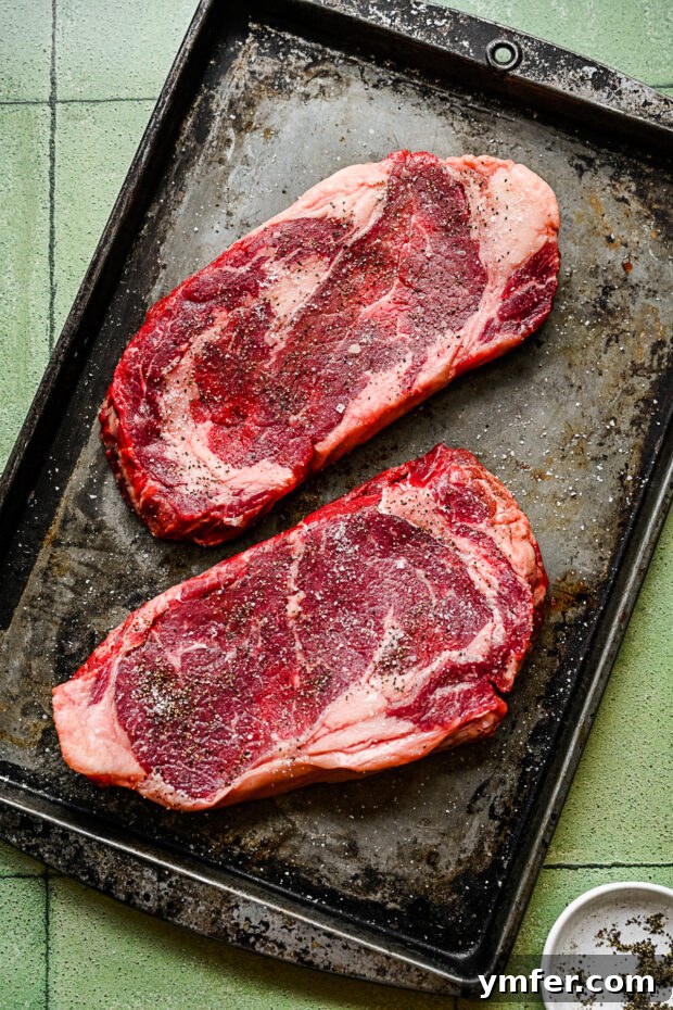 Perfect Pan-Seared Ribeye 5 A raw ribeye steak generously seasoned with coarse salt and black pepper, ready for searing.