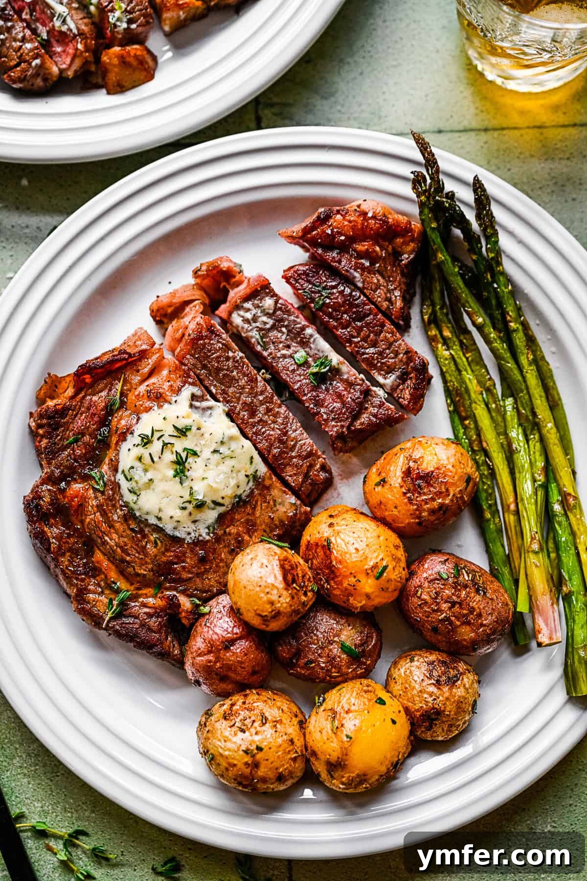 Perfect Pan-Seared Ribeye 7 A perfectly cooked pan-fried ribeye steak, sliced and served on a white plate with roasted asparagus and potatoes.