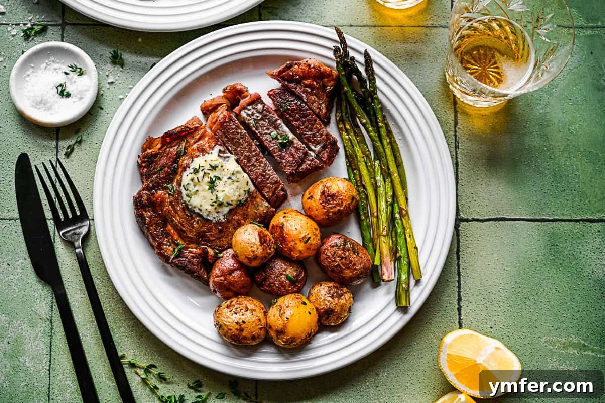 Perfect Pan-Seared Ribeye 9 A pan-fried ribeye steak on a white plate, garnished with fresh herbs, alongside roasted potatoes and green vegetables.