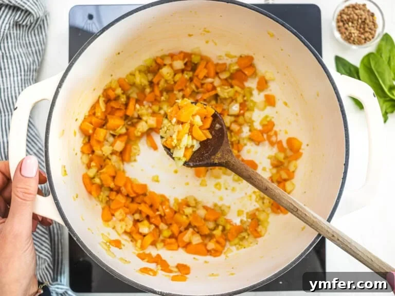 herbs and vegetables in a white Dutch oven and a wooden spoon