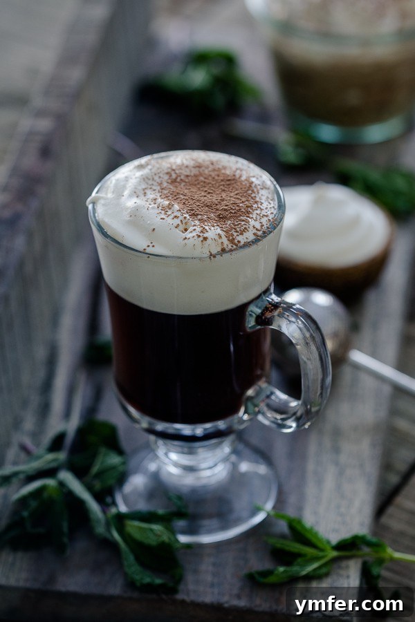 The Quintessential Irish Coffee 2 Traditional Irish Coffee topped with a dusting of chocolate powder, presented in a clear glass mug.