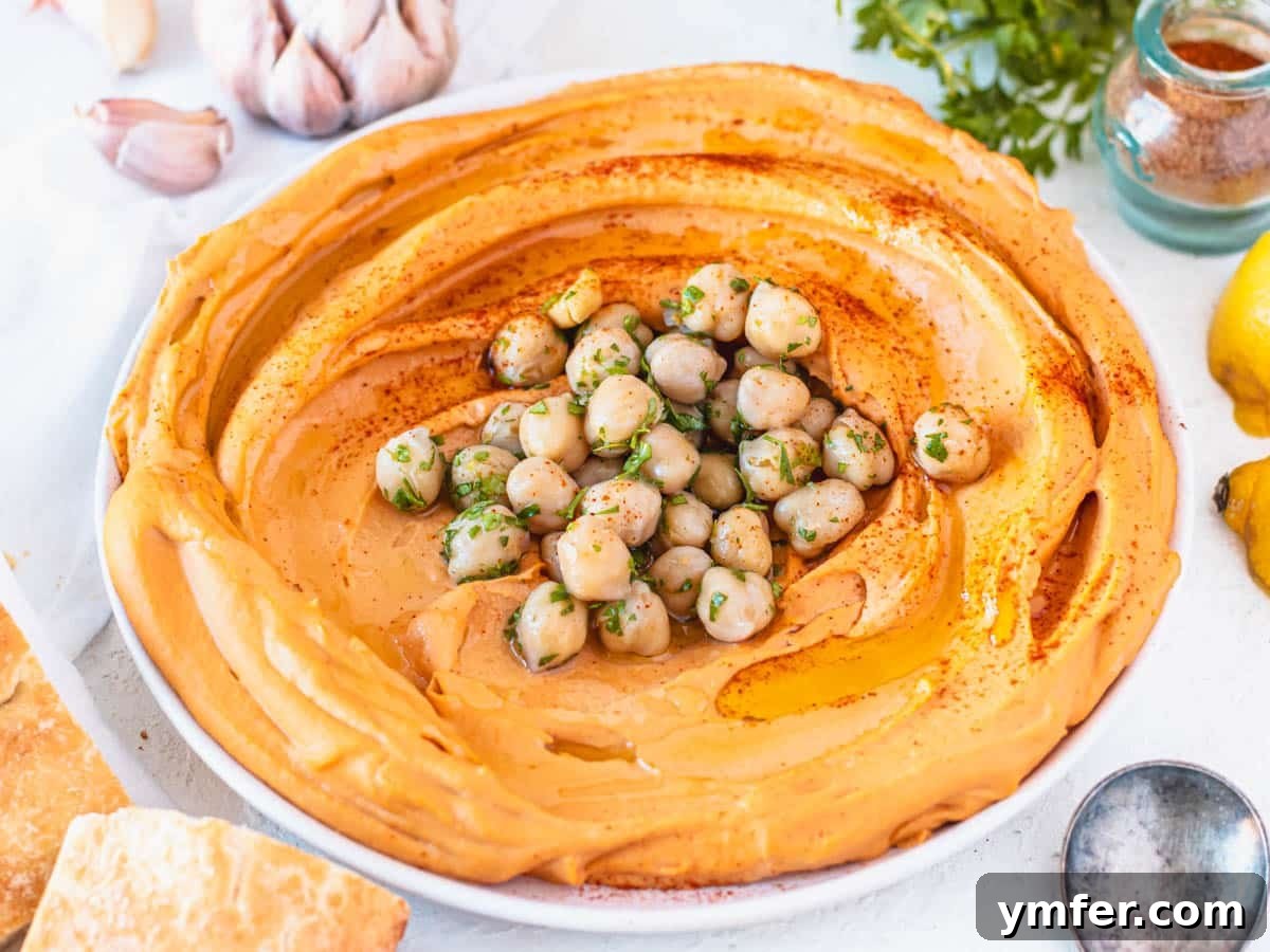 Velvety Roasted Red Pepper Hummus 11 A beautifully presented bowl of roasted red pepper hummus with whole chickpeas in the center and a drizzle of olive oil.