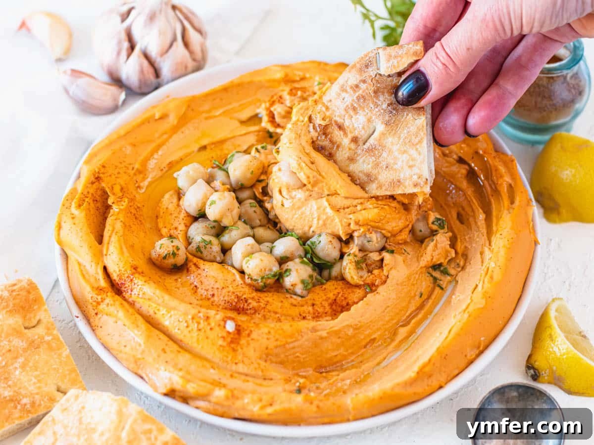 Velvety Roasted Red Pepper Hummus 13 A bowl of spicy roasted red pepper hummus with a piece of pita bread.
