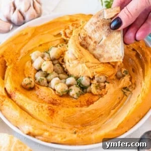 Velvety Roasted Red Pepper Hummus 14 roasted red pepper hummus with chickpeas and hand holding a pita chip