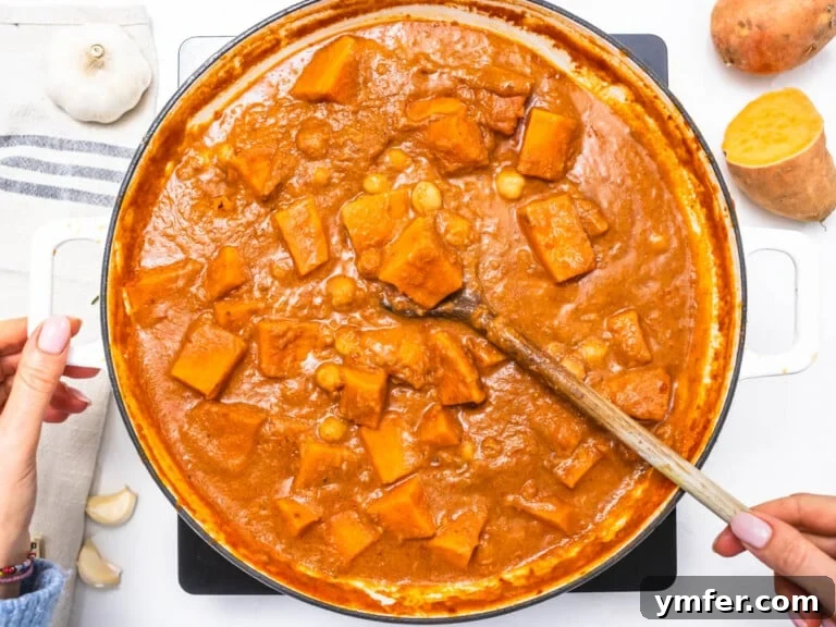 Soulful African Peanut Stew 15 creamy tomato base with sweet potato chunks and chickpeas and hand holding a wooden spoon