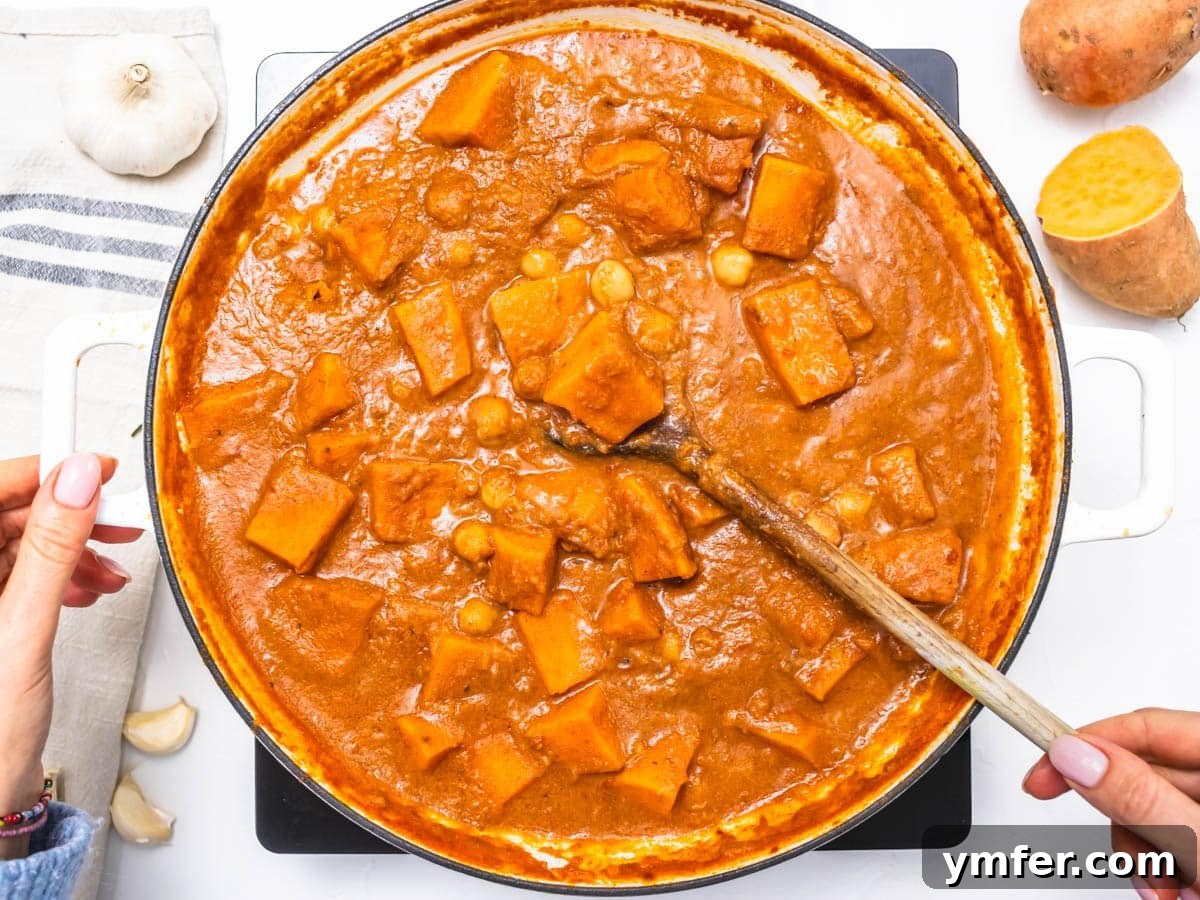 Soulful African Peanut Stew 9 creamy tomato base with sweet potato chunks and chickpeas and hand holding a wooden spoon