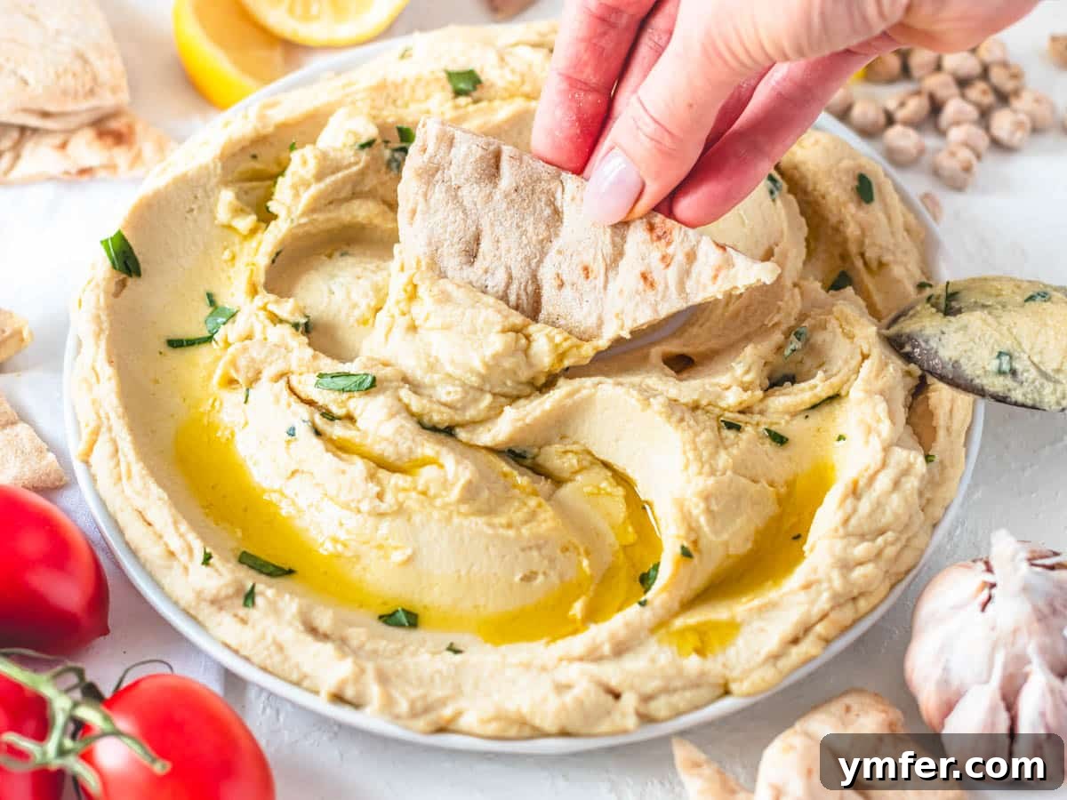 Hummus without tahini on a plate with hand holding a pita chip
