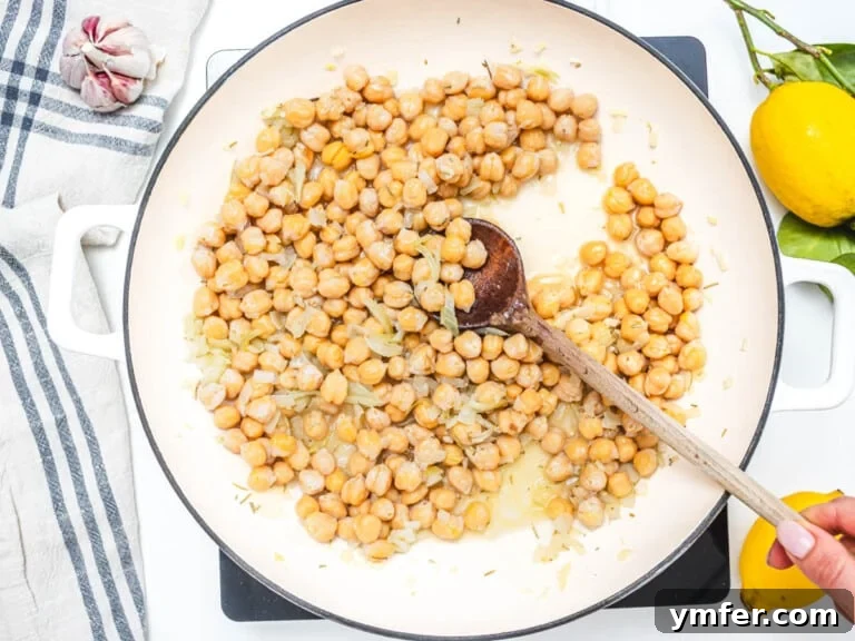skillet with chickpeas and onion and hand holding a spoon