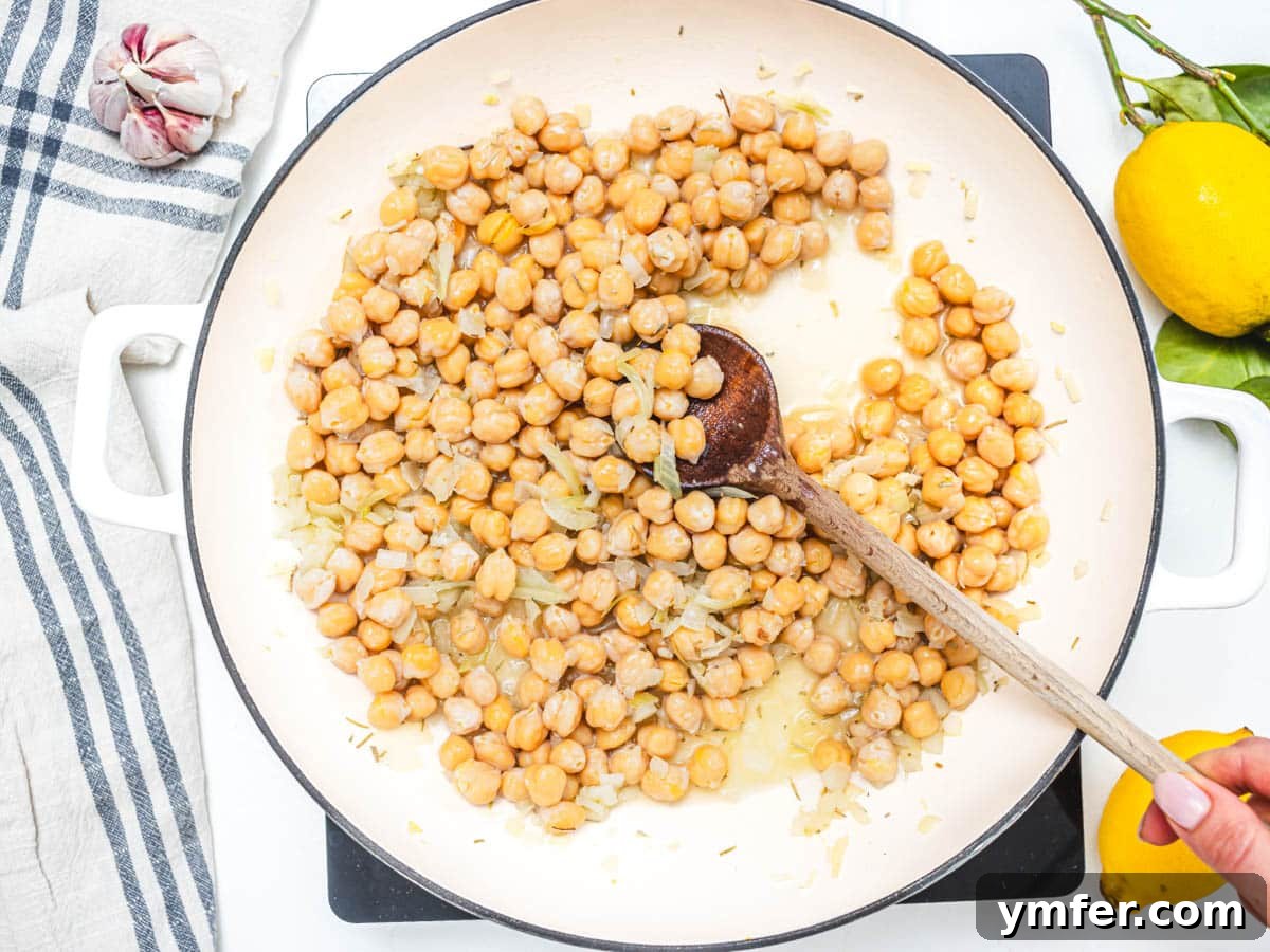 skillet with chickpeas and onion and hand holding a spoon