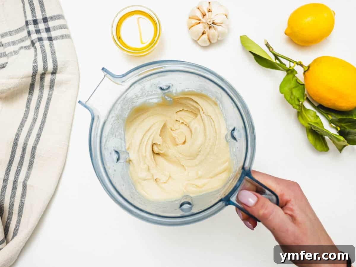 Hummus without tahini in a blender and a hand holding the handle