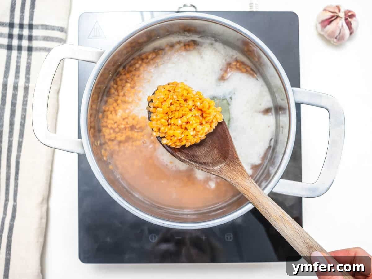 Perfect Red Lentils Every Time 5 Red lentils cooking in a casserole with a wooden spoon, simmering gently