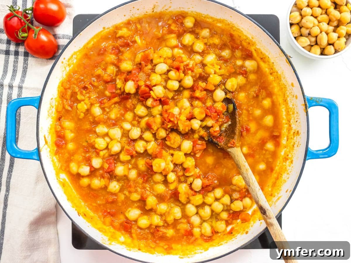 Spiced Chickpea and Spinach Curry 6 Chickpeas and diced tomatoes simmering in a skillet, absorbing the spices and forming the base of the curry.