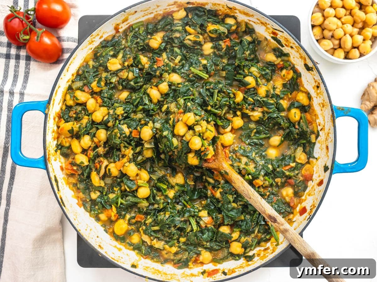 Spiced Chickpea and Spinach Curry 8 A spoonful of fully cooked Chana Saag, showcasing the rich, spiced chickpeas and tender spinach in a blue skillet.