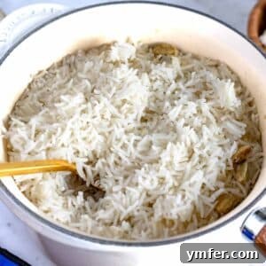 Close-up of fluffy basmati rice in a pot with a golden spoon and scattered cardamom seeds, highlighting its aromatic potential.