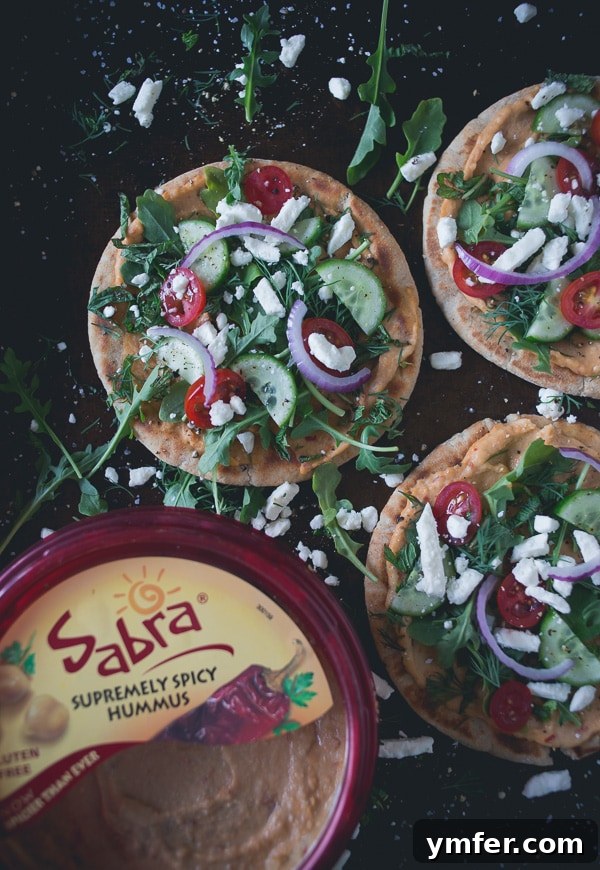 Mediterranean Hummus Pita Pizza 3 Close-up of Greek Salad Hummus Pita Pizza showcasing the layers of spicy hummus, fresh vegetables, and feta cheese.