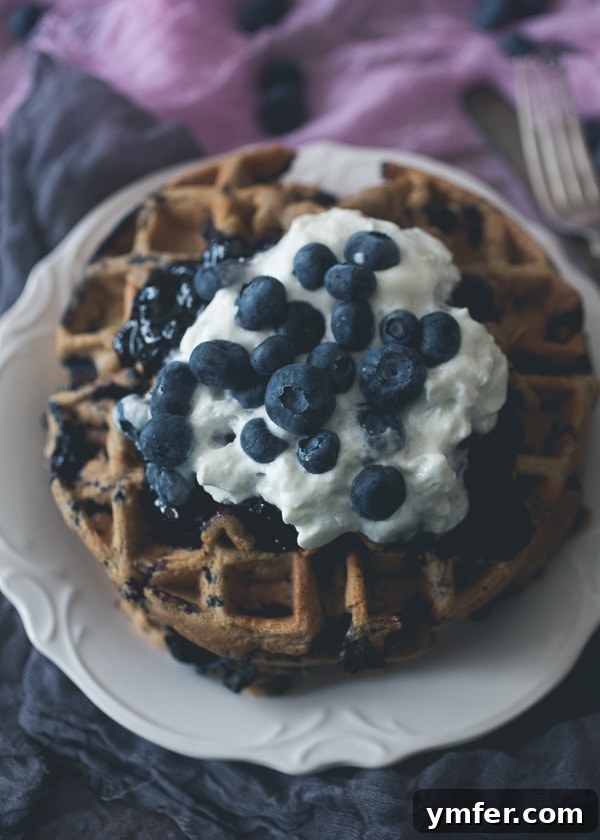 Berry Zucchini Oat Delight Waffles 2 Fluffy blueberry zucchini oat waffles with a dollop of whipped cream and maple compote, perfect for a summer breakfast.