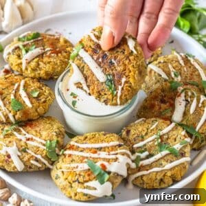 Chickpea fritters with a hand reaching for one and tahini sauce in the background.