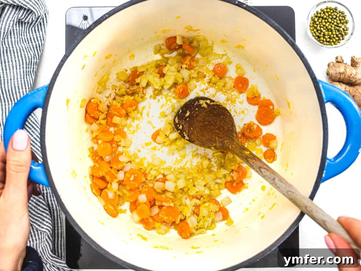 Jade Bean Elixir 7 Carrots and onions sautéing in a blue casserole dish, with hands holding a wooden spoon