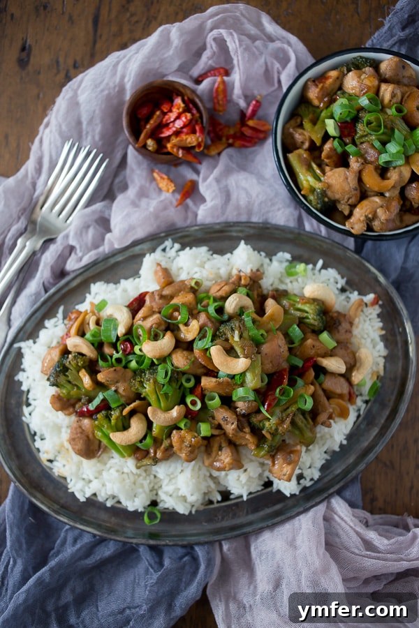 Spicy Cashew Chicken Stir-fry 2 A close-up shot of a plate of vibrant Spicy Cashew Chicken, featuring tender chicken pieces, bright green broccoli florets, and crunchy cashews, all coated in a rich, glossy sauce. Garnished with fresh green scallions and served over fluffy white rice, ready to eat.