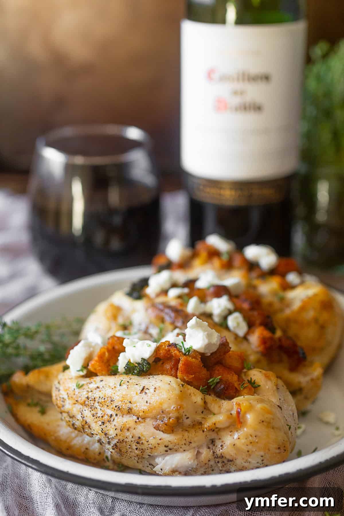 Southern Cornbread Stuffed Chicken 3 Two pieces of cornbread stuffed chicken on a plate, garnished with fresh herbs and a glass of wine in the background.