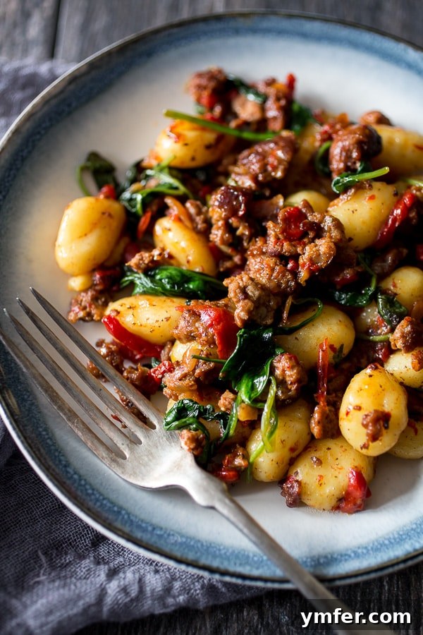 Smoky Chorizo Gnocchi with Roasted Red Pepper and Spinach 4 A fork taking a bite of chorizo roasted red pepper spinach gnocchi from a plate.