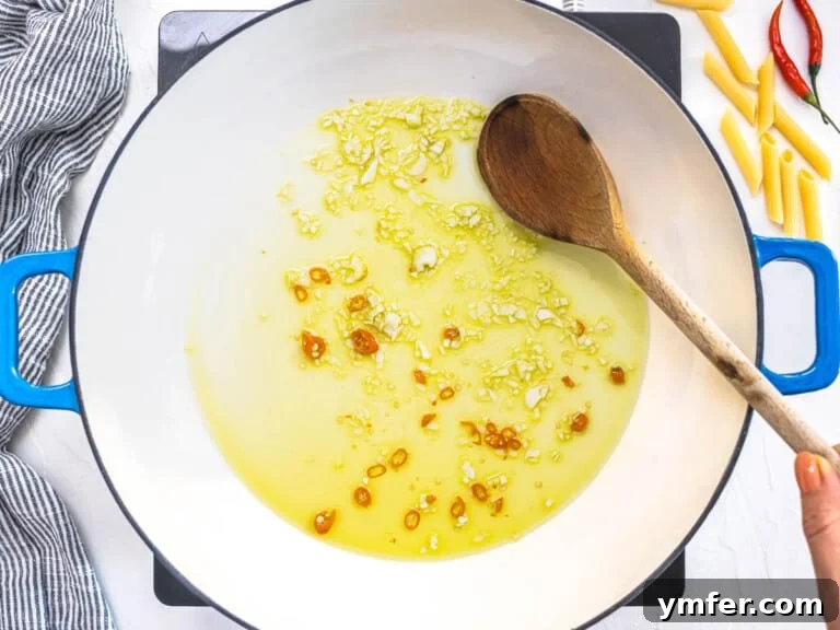 oil, garlic, and chili in a blue skillet with a wooden spoon