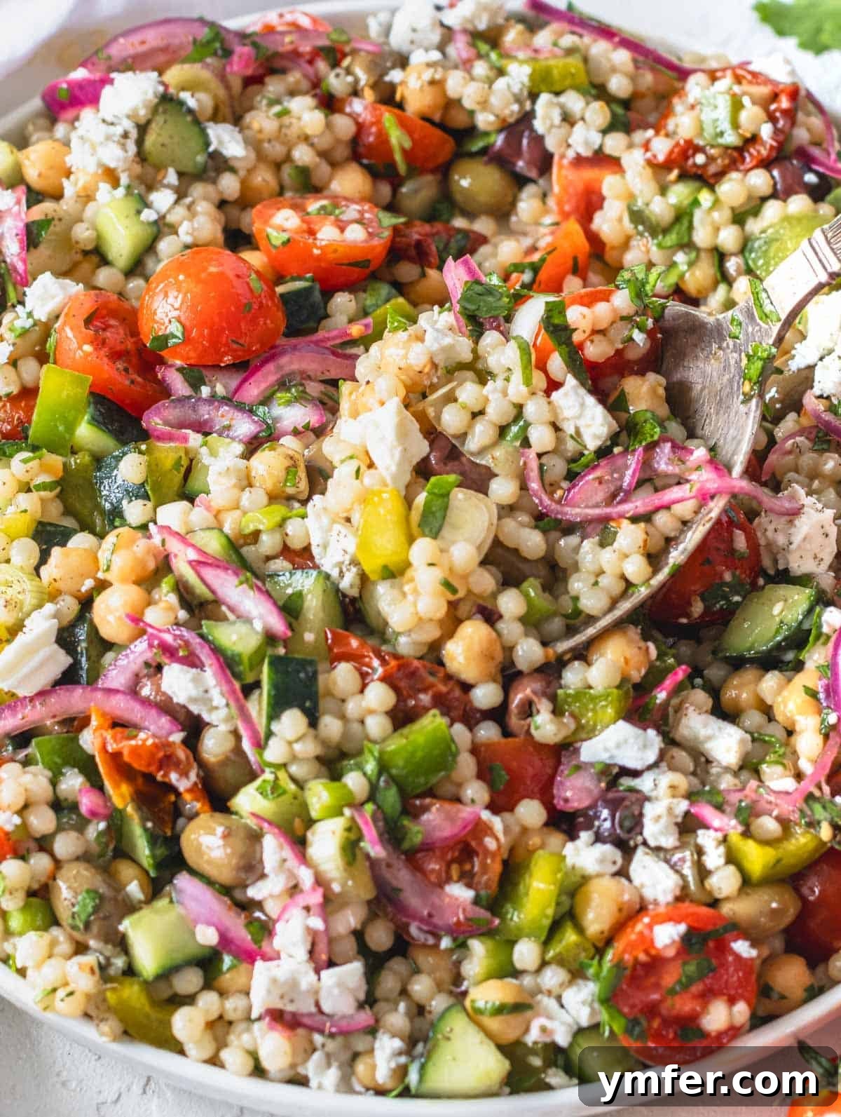 Beautifully plated pearl couscous salad garnished with crumbled feta and fresh herbs.