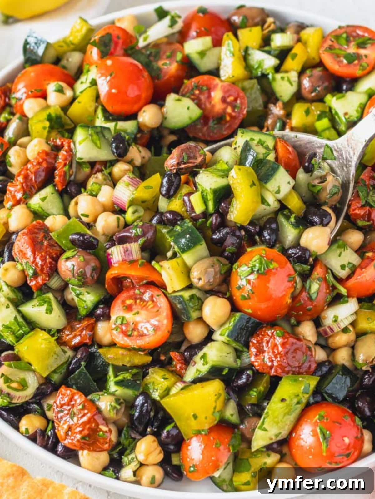 Grecian Summer Salad 2 A colorful Mediterranean salad brimming with chickpeas, black beans, vegetables, and olives, served in a large bowl.