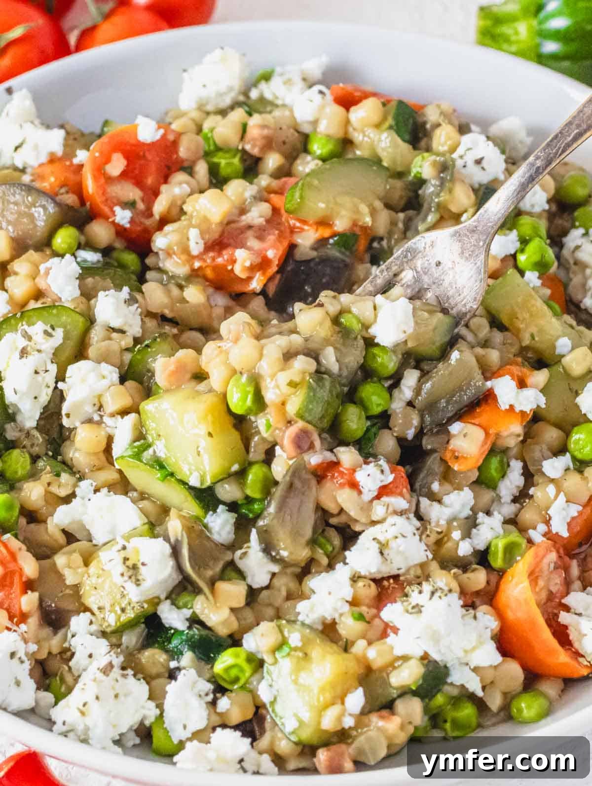 Sardinia's Toasted Pearl Pasta 2 Creamy fregola with vegetables and a silver fork, highlighting the rich texture and vibrant colors of the dish.