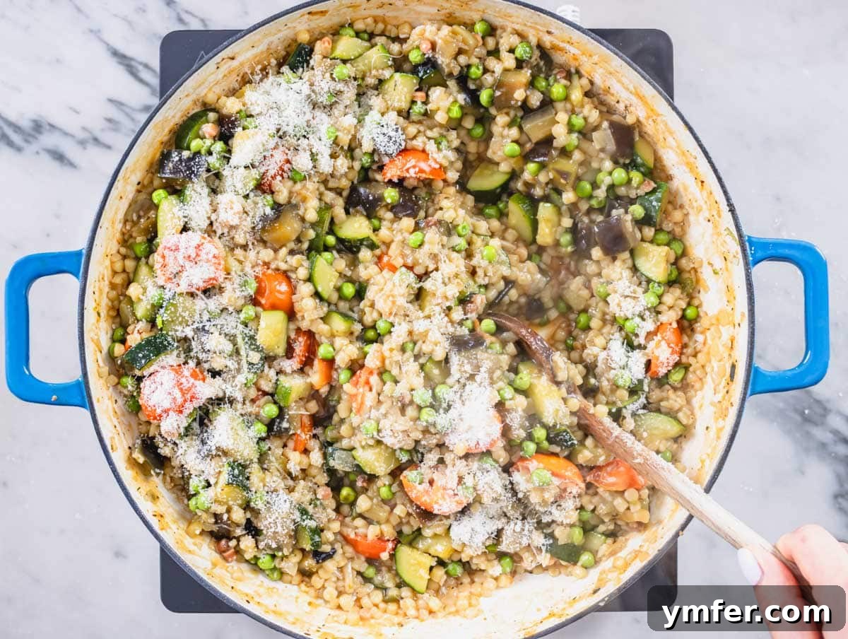 Sardinia's Toasted Pearl Pasta 14 Fregola with vegetables, topped with a generous sprinkle of grated parmesan cheese, ready to be served.