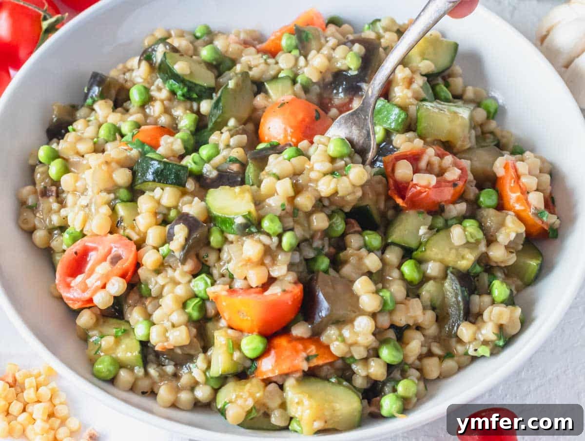 Sardinia's Toasted Pearl Pasta 15 A bowl of creamy fregola with vegetables, ready to be enjoyed with a silver fork.